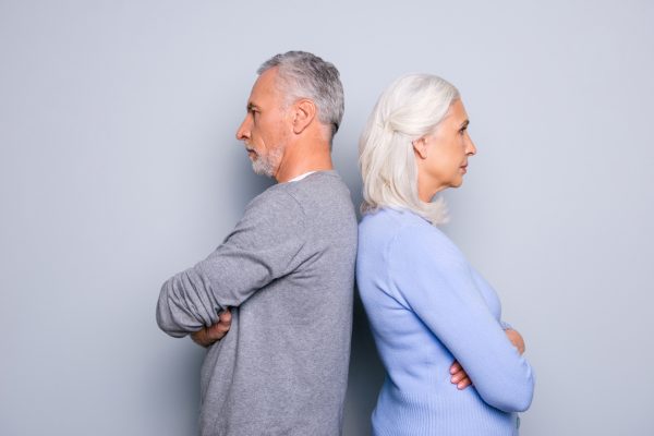 Concept of misunderstanding and  communicative problem between two senior people, they are standing back to back, isolated on grey background