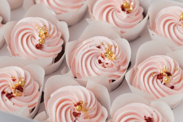 Set of cupcakes with pink whipped cream top decorated with edible golden petals and red dried berries. Close-up shot of cupcakes in the white background. Macro shot