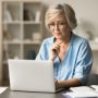 Serious elder senior freelance woman in glasses working at table