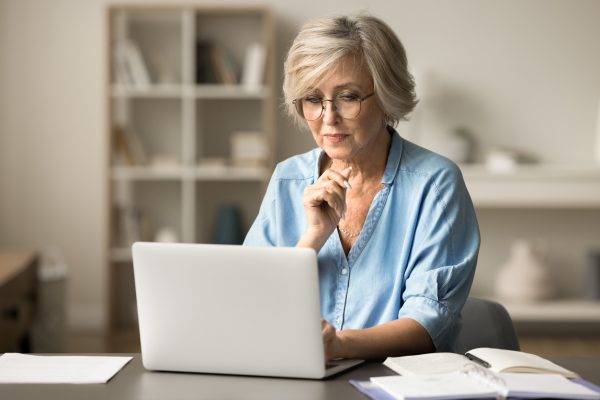 Serious elder senior freelance woman in glasses working at table