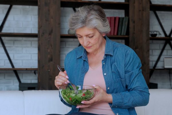 Elderly,Woman,Eats,Her,Vegetable,Salad,Sitting,On,The,Sofa